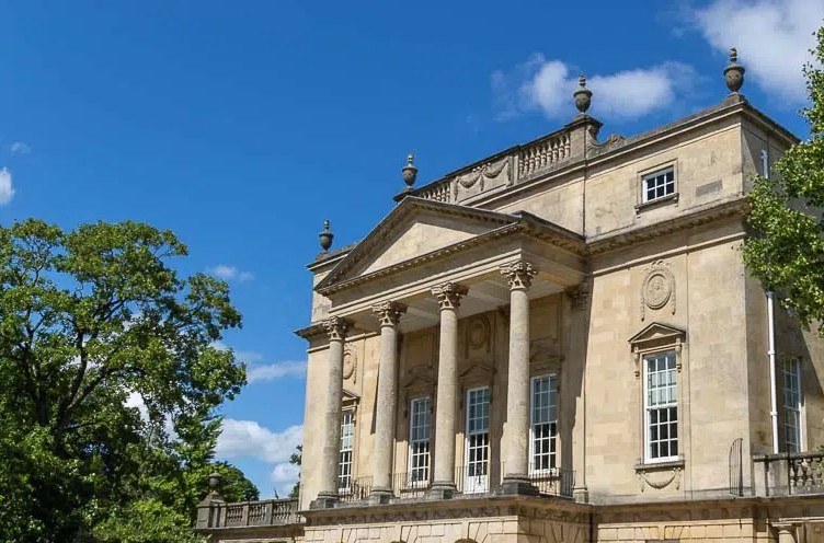 A quiet neoclassical Bath stone building framed by trees.